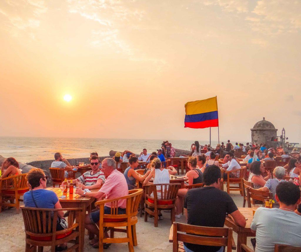 Por do sol no Café del Mar com pessoas sentadas nas cadeiras e bandeira colombiana hasteada